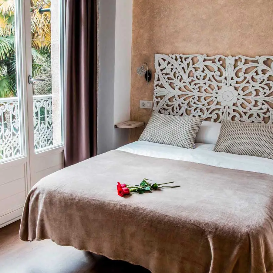 Habitación 102: cama de matrimonio con cabecero blanco tallado junto a la puerta del balcón