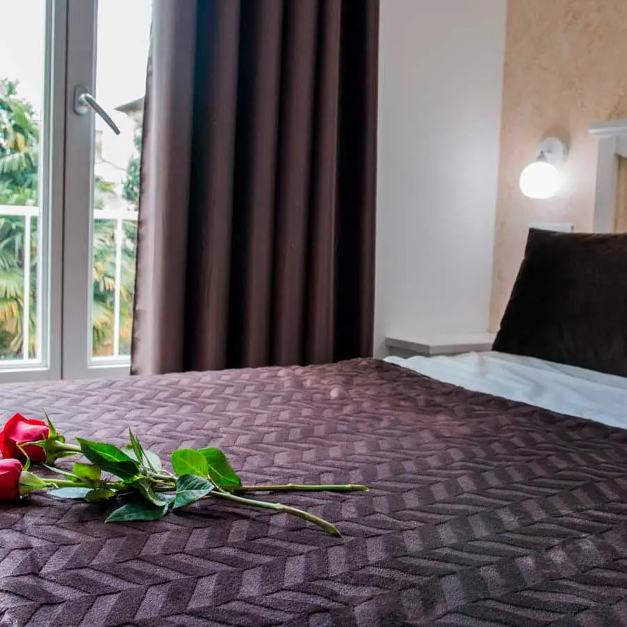 Habitación 202: cama de matrimonio con rosas sobre la colcha y la puerta del balcón al fondo