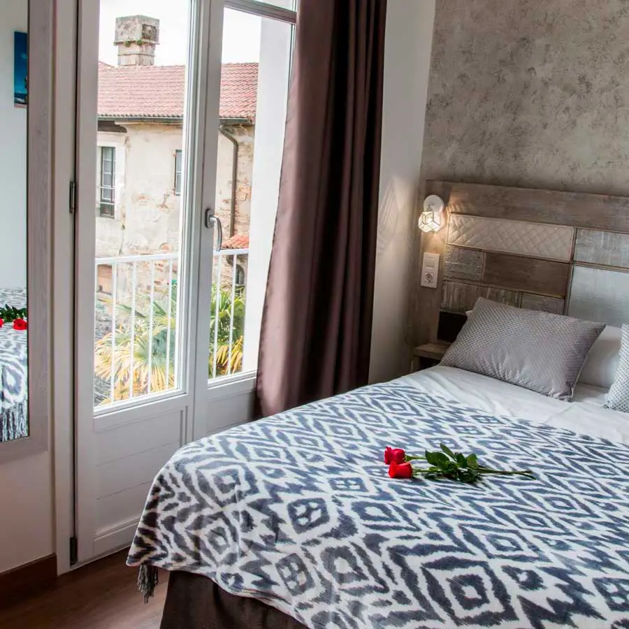 Habitación 302: cama de matrimonio con colcha estampada junto a la puerta del balcón