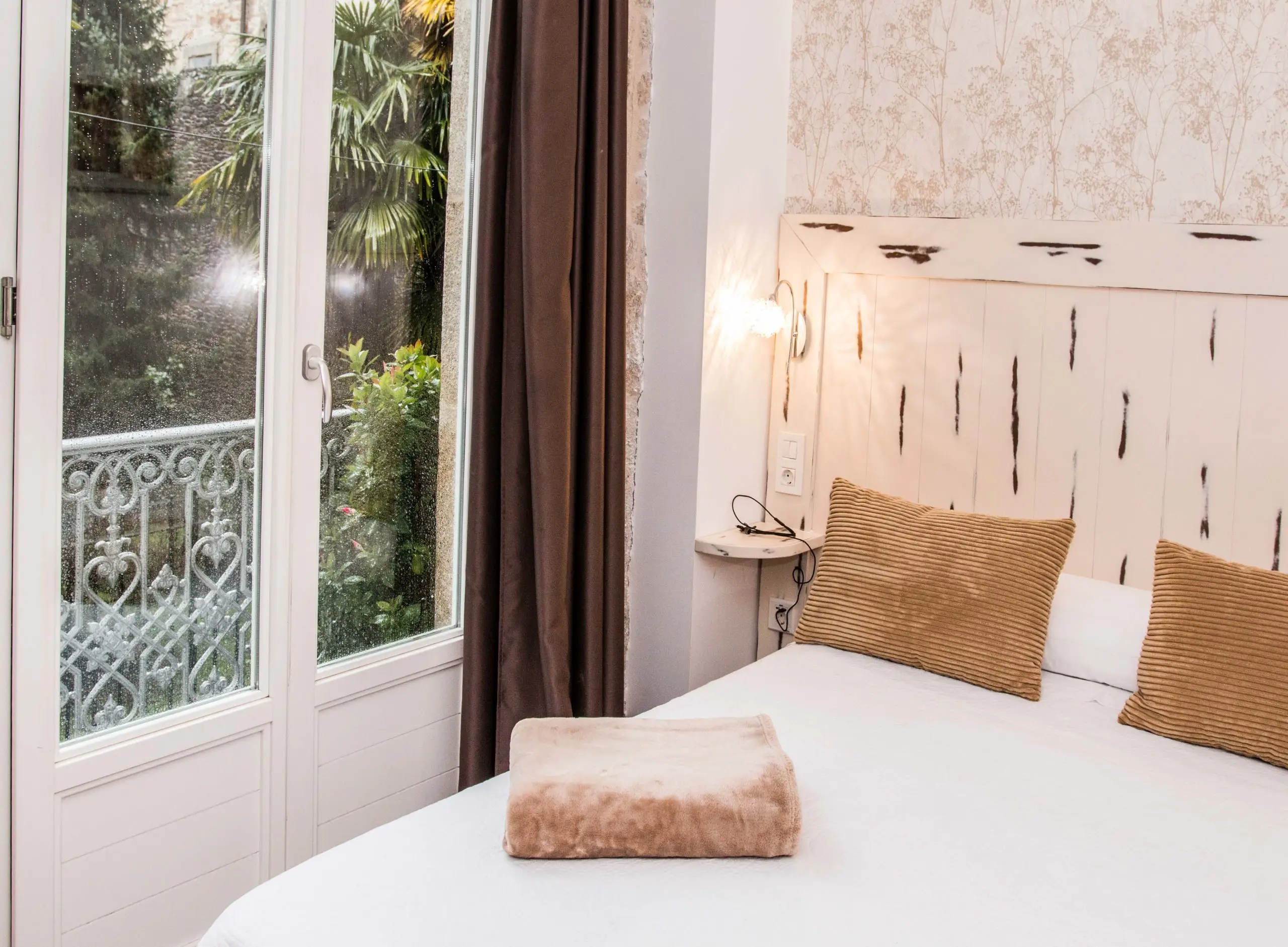 Habitación con cama de matrimonio y puerta acristalada al balcón, con la lluvia en los cristales